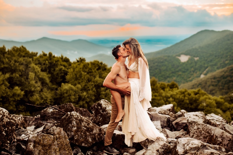Family Photographer, a man and woman kiss on mountain rocks before the forests